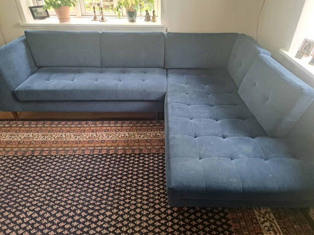 Blå sofa før rens med pletter og skjolder i stoffet